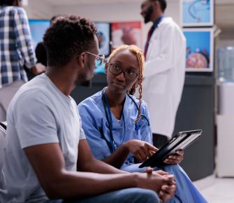 Male patient with female clinician in medical reception who is holding an ipad