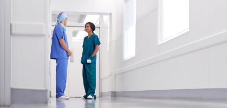 two nurses in scrubs talking in hospital corridor 
