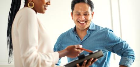 A female clinician holding a tablet, showing their smiling male patient 