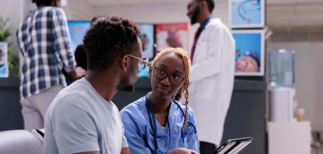 Male patient with female clinician in medical reception who is holding an ipad