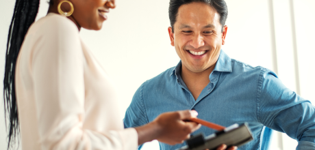 Female clinician holding a tablet and pointing to the screen with a pen while explaining information to a smiling male patient.