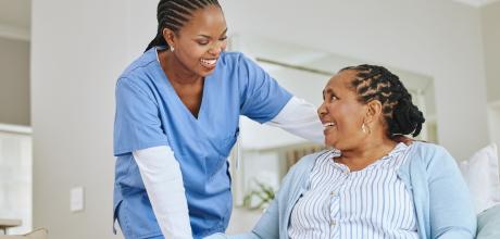 Clinician smiling to a woman sat in a chair, who is looking up at her and smiling back