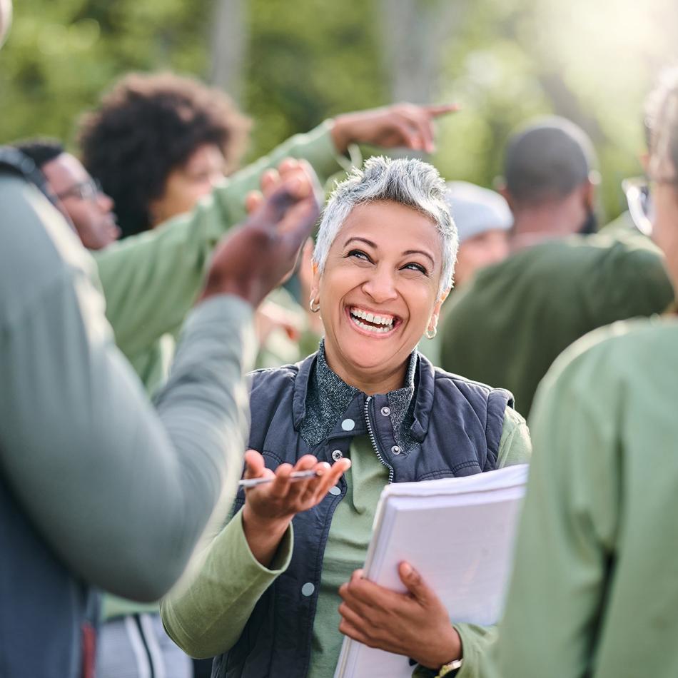 Photograph: Smiling woman with grey hair conversing animatedly with a group outdoors.