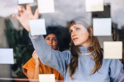 Photograph: Two women intently arranging yellow sticky notes on a glass screen.