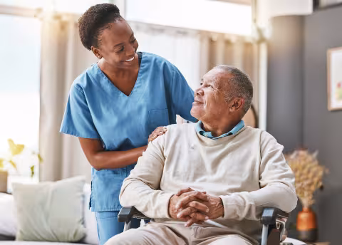 Nurse wearing blue scrubs with elderly man in wheelchair 