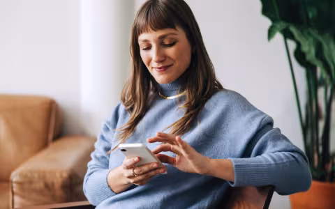 Woman sat on a chair, touching the screen on her phone