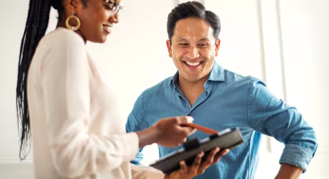 A female clinician holding a tablet, showing their smiling male patient 