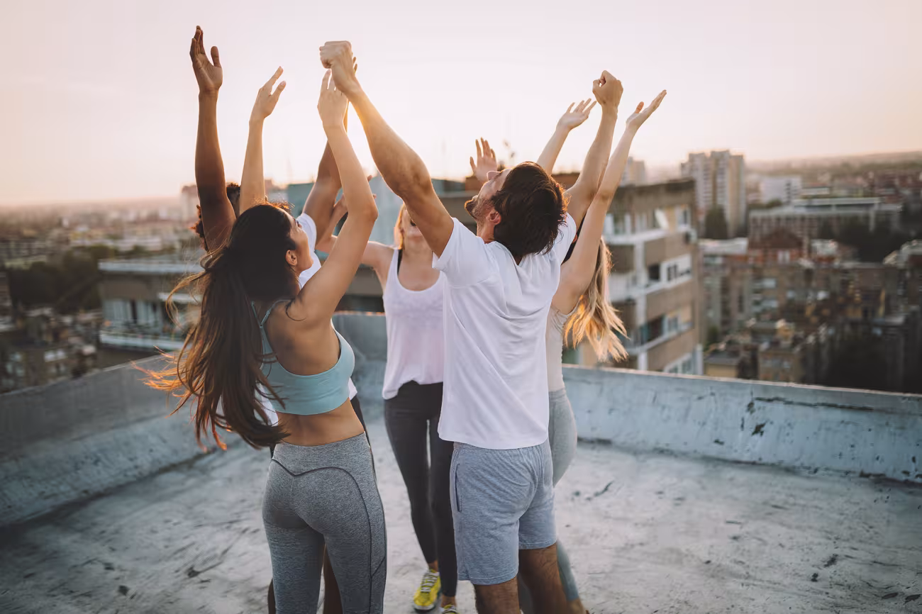 Joyful group raising arms on a city rooftop at sunset.