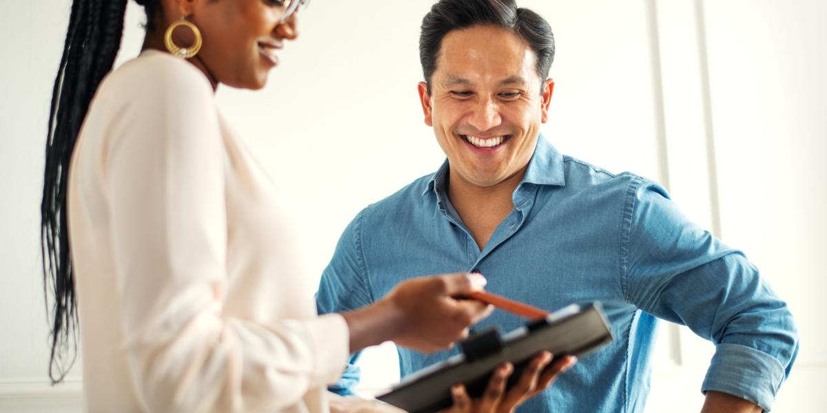 A female clinician holding a tablet, showing their smiling male patient 