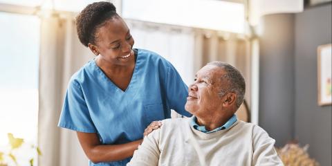Nurse wearing blue scrubs with elderly man in wheelchair 