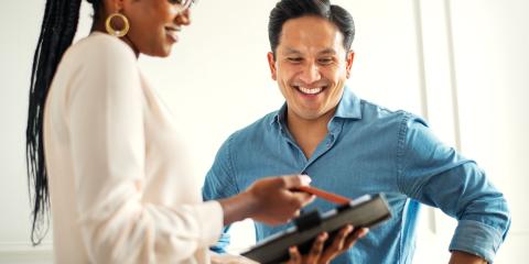 A female clinician holding a tablet, showing their smiling male patient 